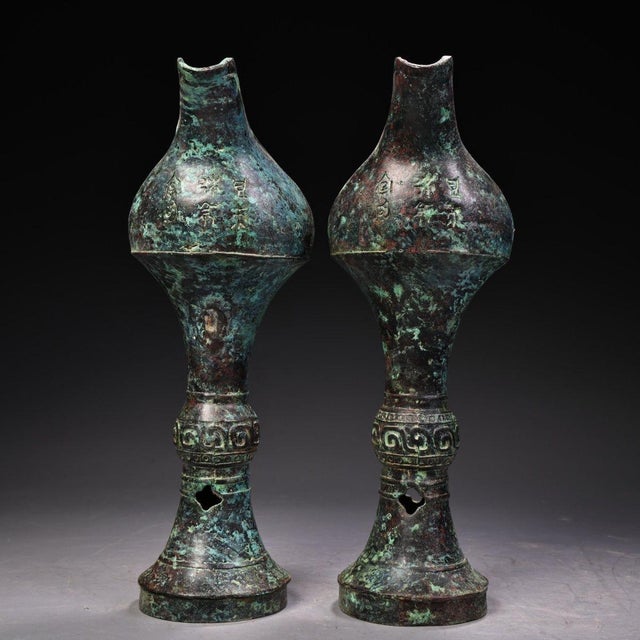 This is a matching pair of cast bronze stemmed cups, each featuring a bulbous upper body that tapers into a slender stem...
