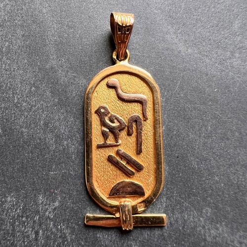 An 18 karat (18K) yellow gold charm pendant designed as an elongated rectangular tablet with Egyptian heiroglyphics....