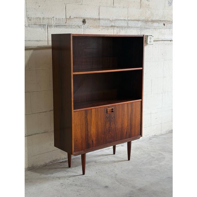 This elegant mid-sized Bookcase features an upper open display shelving unit standing above a lower cabinet compartment....