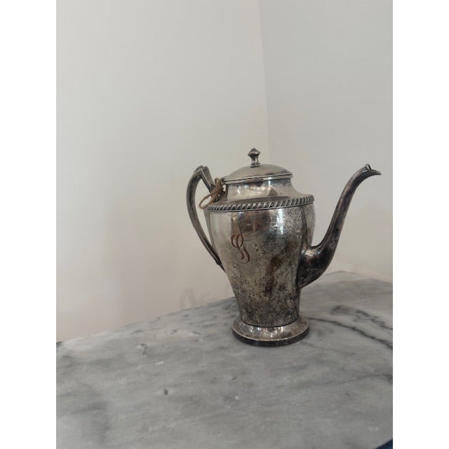 Elegant vintage silver-plated coffee pot featuring a classic tapered silhouette, graceful curved spout, and decorative...