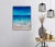 This mixed media artwork depicts the dynamic interplay of ocean waves meeting a sandy shore, rendered in vibrant shades of...