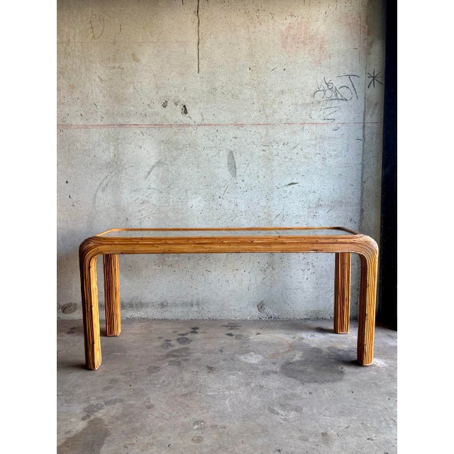 This striking vintage pencil reed console table dates to the 1970s and features an elegant waterfall silhouette with four...