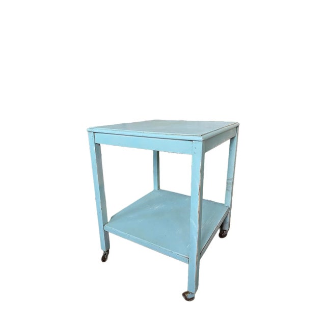 A wooden painted side table that is a pretty aqua color and it has wheels. It is a vintage piece from the 1950's.