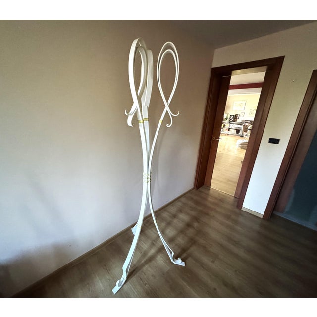 Unique hand-forged iron coat stand with a sculptural, column-like silhouette, finished in white with subtle antique gold...