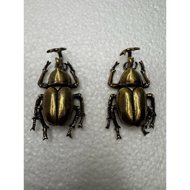 The vintage pair of solid brass knobs are crafted in the form of stylized rhinoceros beetles, featuring detailed legs,...