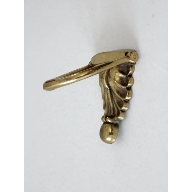 This is an antique brass door knocker with a distinctive scalloped crest and sconce-like silhouette. The decorative...