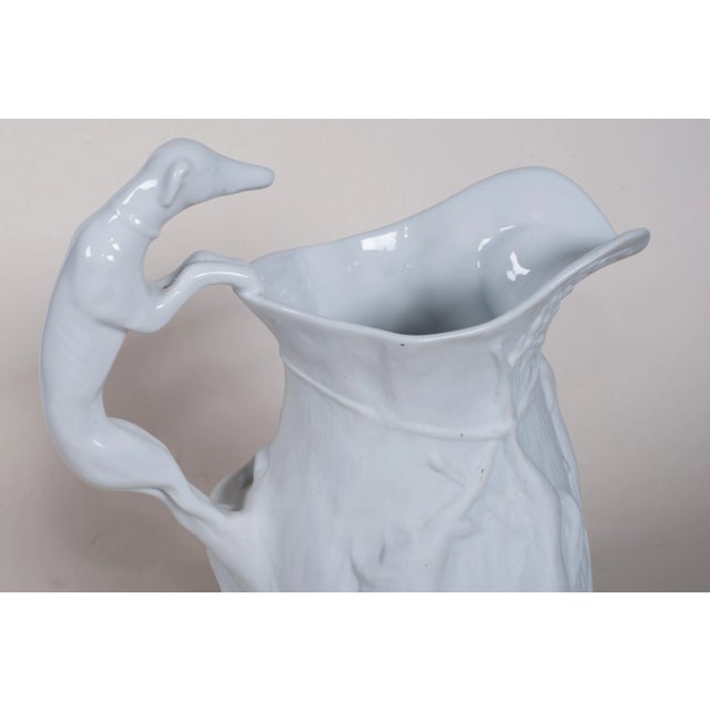 Pitcher has hound handle and trussed up rabbit, birds, foliage in relief. It is glazed inside. Biscuit finish on the outer...