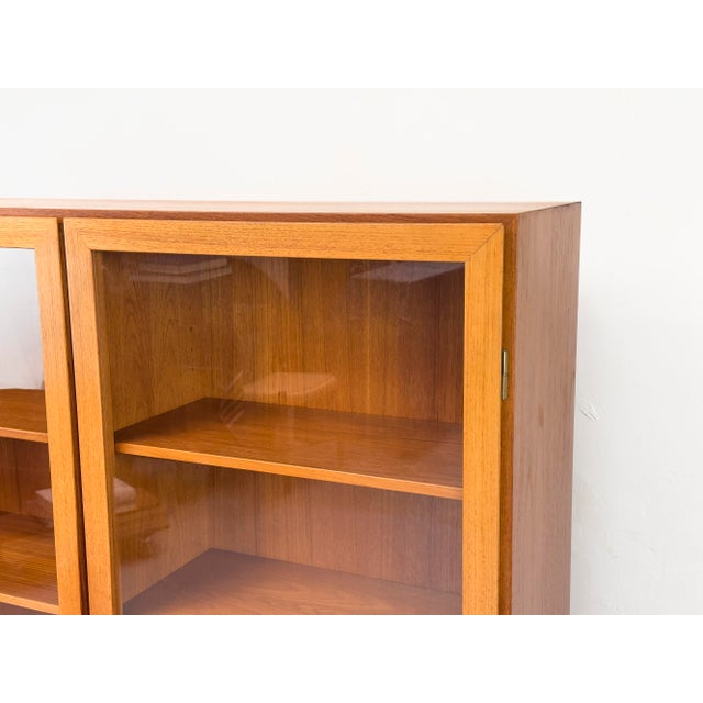 High-quality mid-century display cabinet by Omann Jun from the 1960s. Teak-veneered body with solid teak and glass doors....