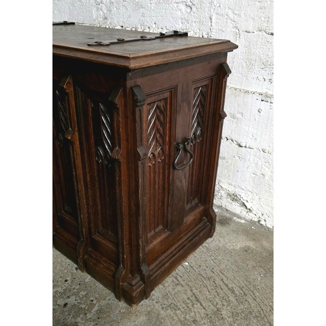 A 19th-century carved oak chest in the Neo-Gothic style. The front is punctuated by vertical carved panels decorated with...