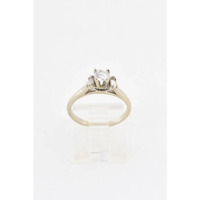Elegant 14K white gold ring presenting a .35 carat diamond mounted in a traditional four-prong setting flanked by a...