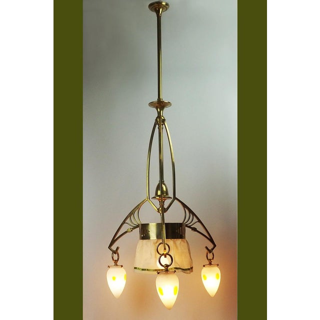 High circular brass chandelier with three lights filtered by opalescent white glass warheads decorated with irregular...