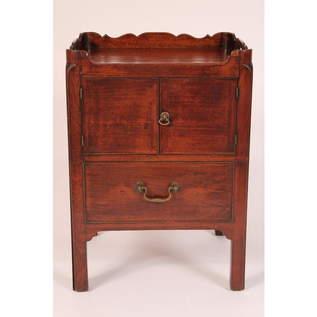 George III mahogany bedside table, circa 1790. The mahogany top with back and side scalloped gallery with carrying...