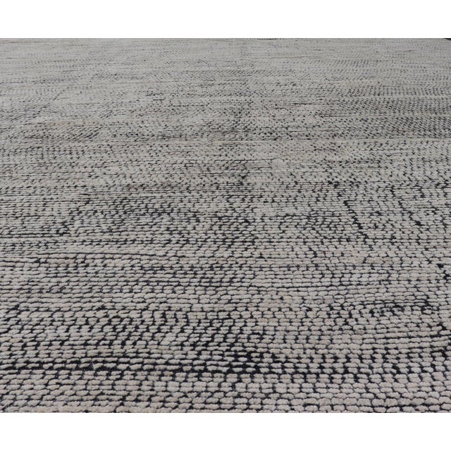 This large modern casual rug's field displays a ivory colored pile. Underneath the field shows a black base for a...