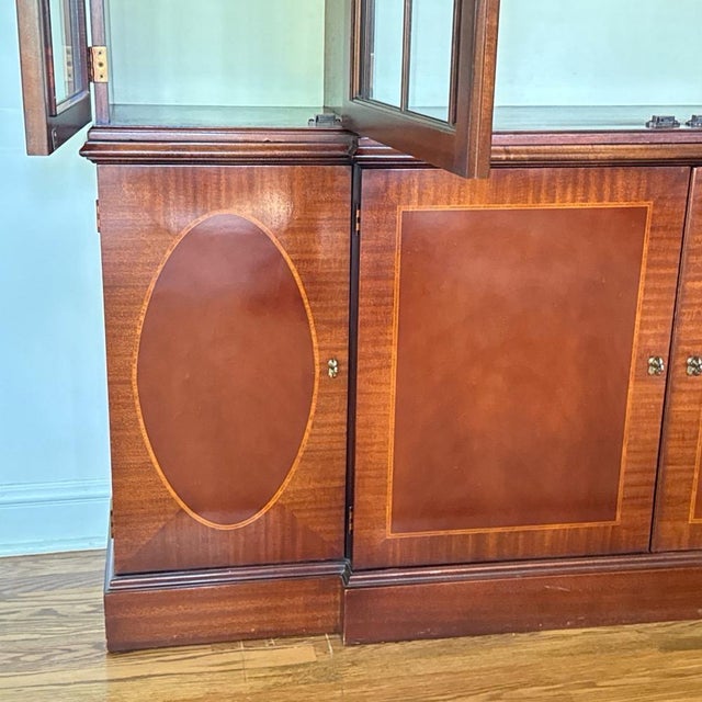 A vintage Baker Georgian style lighted mahogany breakfront china cabinet with a stepped cornice, four-door astragal glazed...