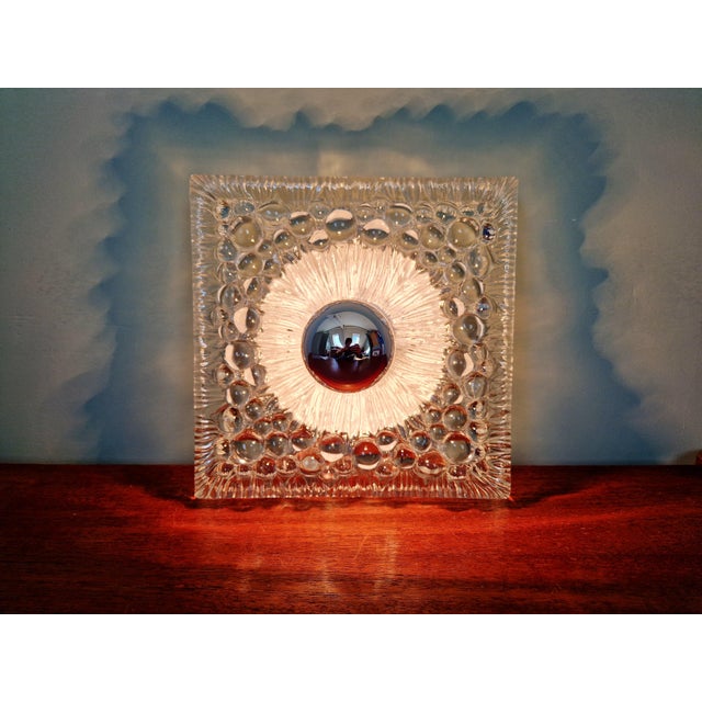 Space Age wall sconce in clear pressed molded glass with a white lacquered metal base, 1970s. The sconce is compatible...