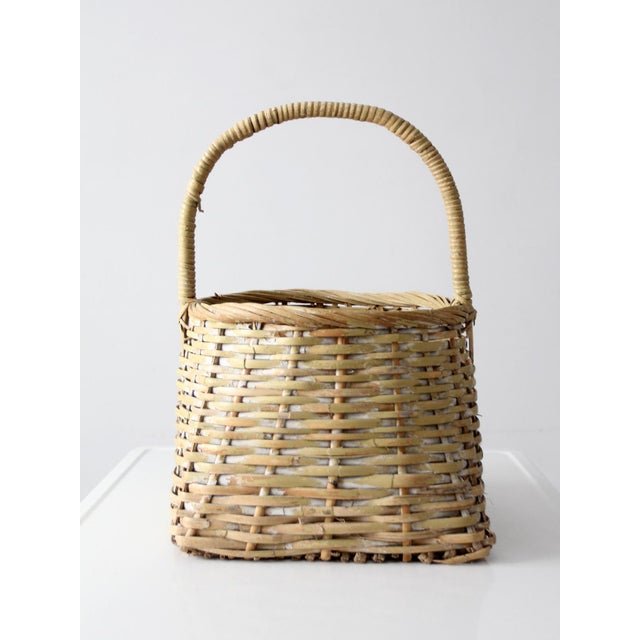 Vintage handmade basket with a softly tapered form and an arched handle. The open, rhythmic weave reveals layered tones of...
