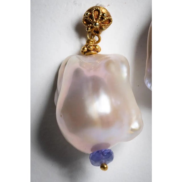 A pair of baroque pearl earrings with a faceted tanzanite gemstone bead at the bottom and 22K gold post and beads. For...