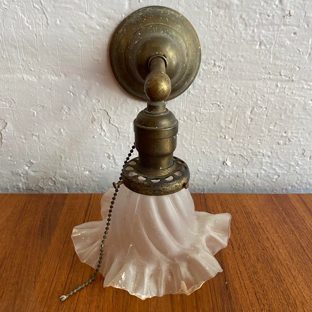 Dating from the early 20th century, this early industrial wall sconce pairs a solid brass pipe arm with an elegant ruffled...