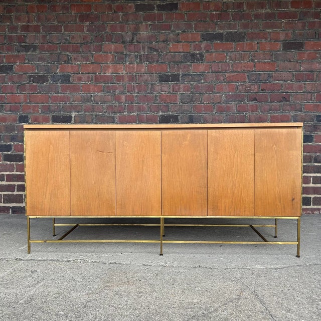 This Paul McCobb credenza has thin and elegant brass stretchers and legs. The trifold doors open up to two drawers and...