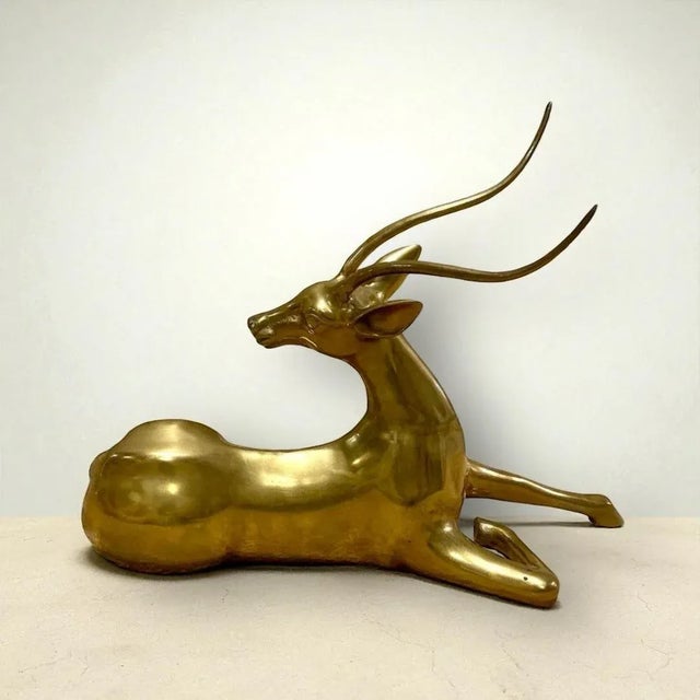 This Vintage Cast Brass Gazelle Statue captures a streamlined and elegant silhouette of a reclining gazelle, crafted in...