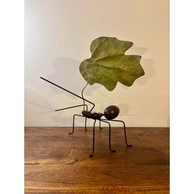 This sculptural metal work depicts a finely rendered ant in motion, carrying a broad green leaf across its back. Executed...