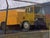 Street Sweeper by Brad Davis | Oil on panel Yellow street cleaning vehicle behind a fence. For Sale