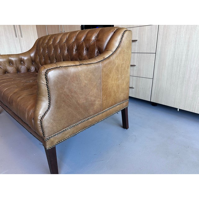 Richly upholstered in warm camel-tone leather, this classic Chesterfield-style loveseat features deep diamond tufting,...