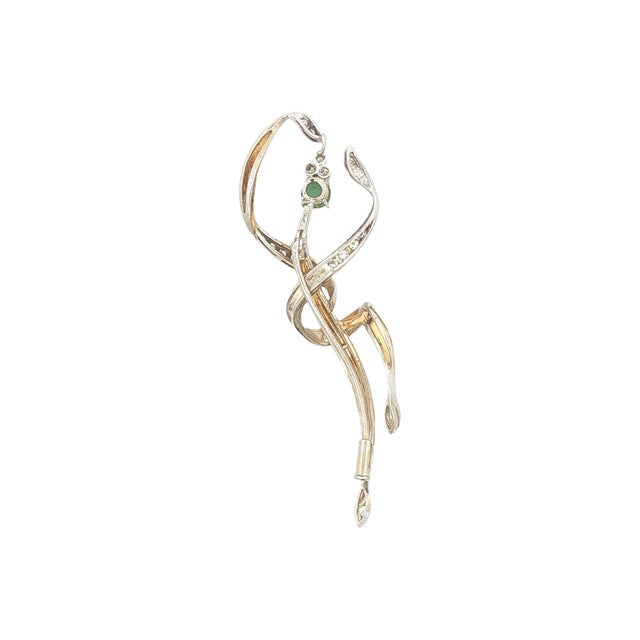 A modern 18k gold brooch featuring a cabochon-cut green emerald. The design includes intertwined gold and diamond-...