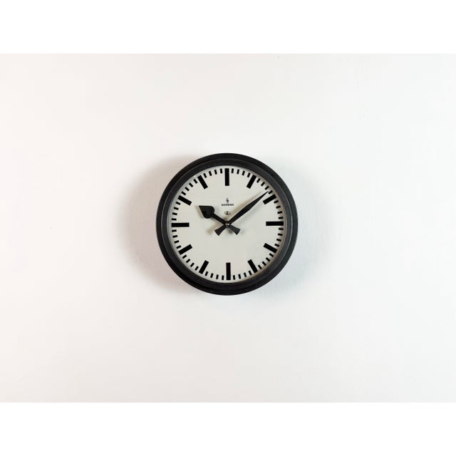 This wall clock was produced by Siemens in Germany during the 1950s. It features a black metal frame, a metal dial and a...