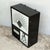 A wall-mounted optician's test cabinet in a black-painted wooden case. Behind a hinged front frame there are three...