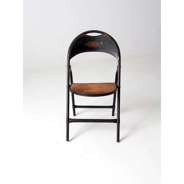 A vintage early 20th century metal folding chair featuring a black painted frame and a brown velvet upholstered seat. The...