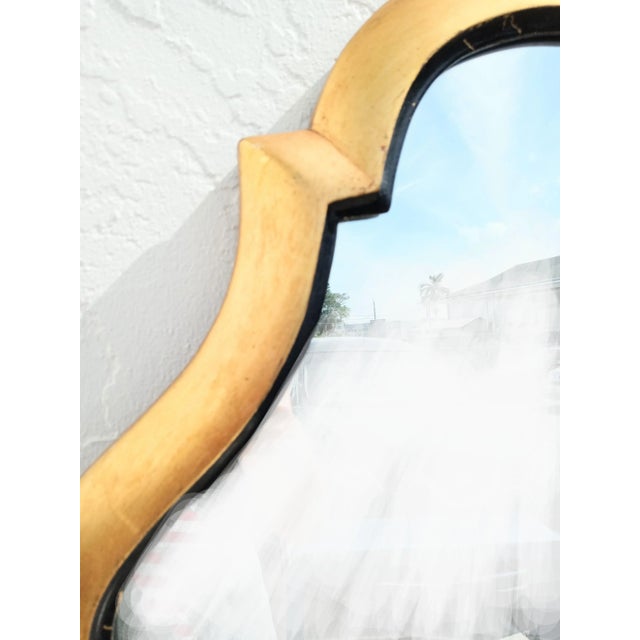 A beautiful and unusually shaped wall mirror by John Stuart. The mirror features a gold leaf frame with black trim. It can...