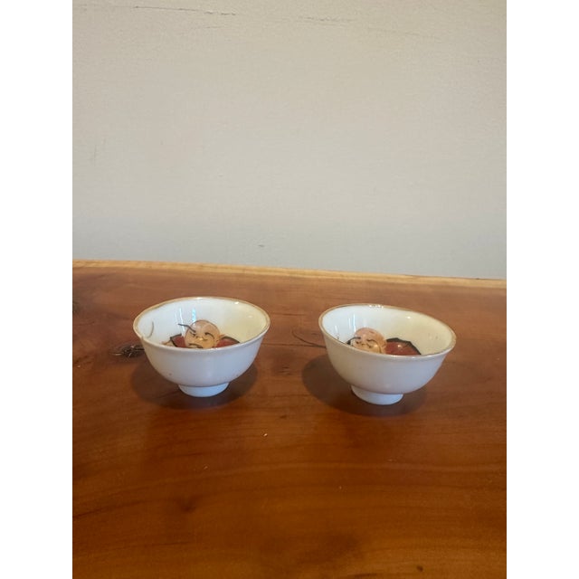 A sweet pair of small porcelain bowls, each featuring a hand-painted figure nestled inside. Simple on the exterior with a...