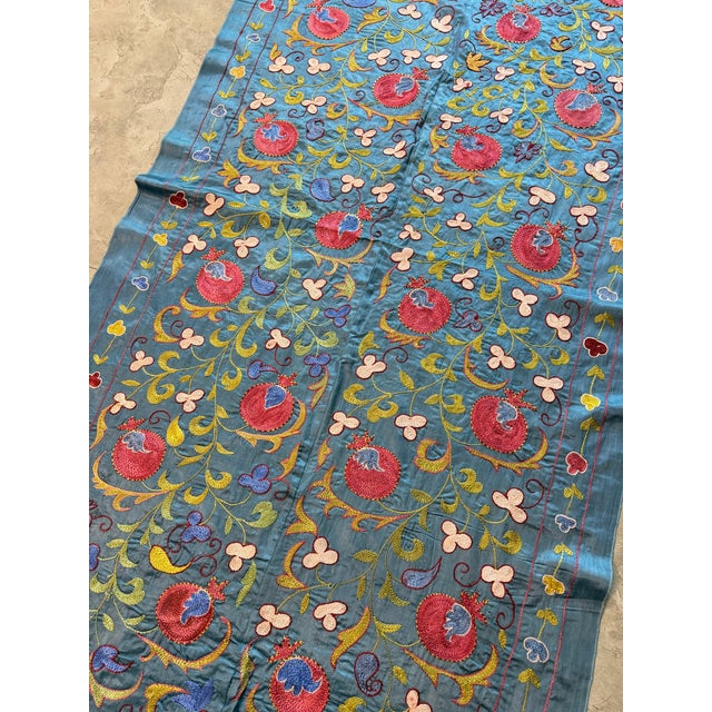 Hand-embroidered Suzani panel from Uzbekistan — red pomegranates and cream trefoil blossoms scrolling over a teal blue...