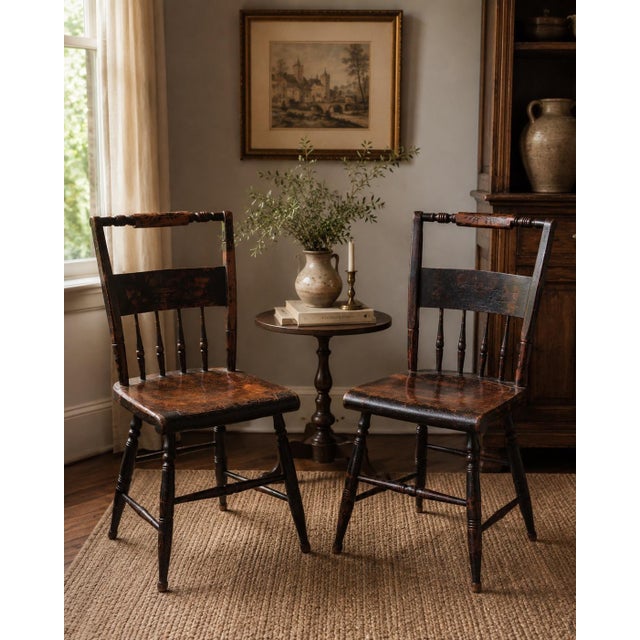Charming pair of antique spindle-back side chairs featuring a beautifully aged dark painted finish with warm reddish-brown...