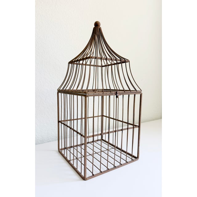 A charming decorative wirework birdcage featuring a tiered pagoda-style dome top and a weathered brown-bronze painted...