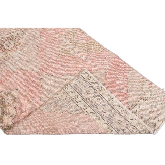 Beautiful vintage Turkish hand-knotted wool rug with a pink and beige field. This rug has accents of ivory and brown in a...