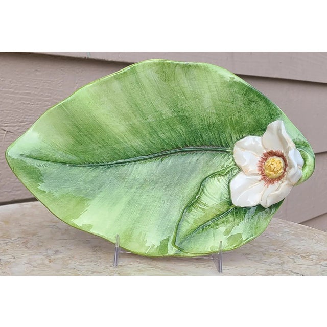 This is a contemporary trinket tray in the Italian majolica style. A single white flower accents a large leaf as its...