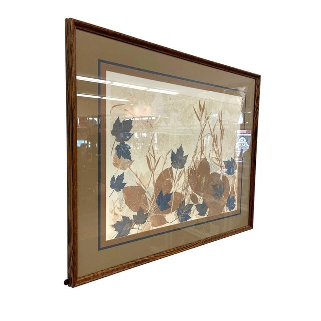 This decorative vintage framed artwork features a stylized botanical composition of layered leaves and grasses in muted...