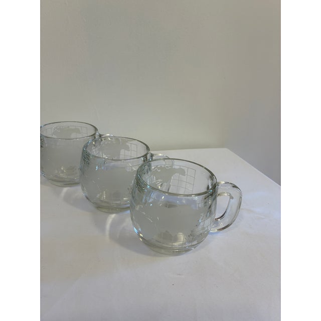 A set of six vintage Nestlé glass mugs dating to the 1970s. Each clear glass mug features an etched world map motif...