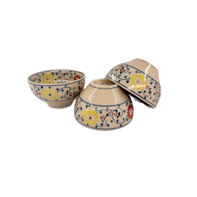 A cheerful set of three hand-painted ceramic bowls from Bat Trang, Vietnam, decorated with a colorful floral pattern that...