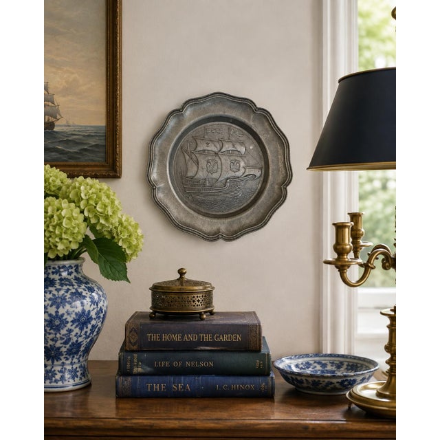 A handsome mid-20th-century German pewter wall plate featuring a fully rigged sailing ship in raised relief, its sails...