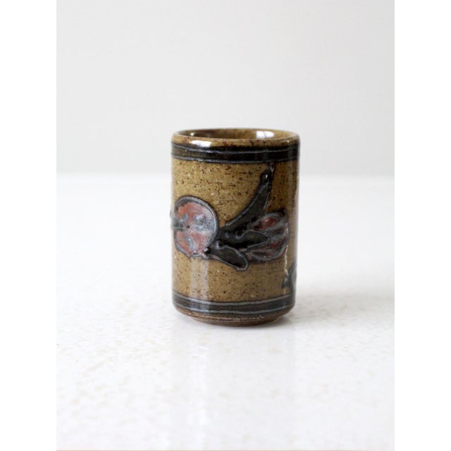 This mid-century Otagiri stoneware cup features a cylindrical form with a textured floral relief, finished in earthy red...