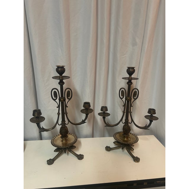 A pair of French Empire style bronze candelabras with ornate scrollwork and tripod bases. Lion’s paw feet. Each measures...