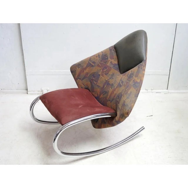 This rocking chair from the 1970s features a chrome construction and fabric and natural leather upholstery.