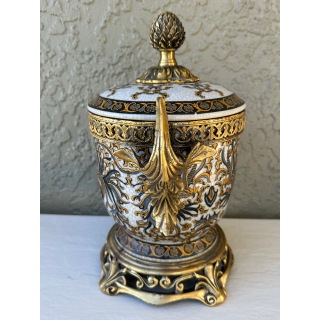 Vintage decorative urn made of porcelain with brass mounts. This ornate urn features a crackled white porcelain body with...