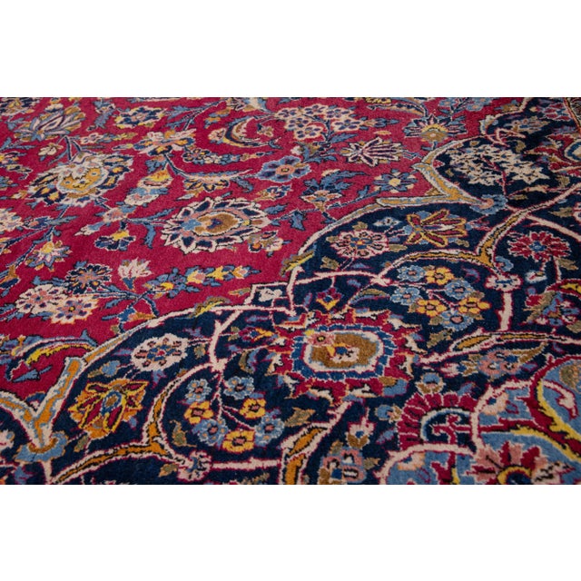 This antique Kashan wool rug boasts an exquisite design, featuring a red color field and a distinguished blue frame...
