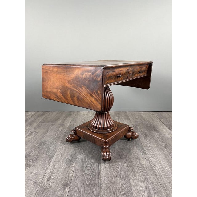 An elegant drop-leaf table in mahogany and mahogany veneer, resting on a central base carved in the shape of a fluted...