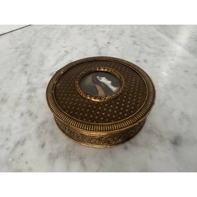 A lovely antique French trinket box constructed of brass having a hand painted portrait in the center. The brass on the...