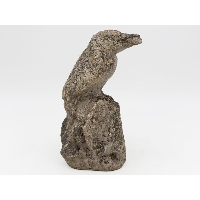 Poised on a rugged stone base, this perched bird figure has a striking, sculptural silhouette, with an alert, slightly...